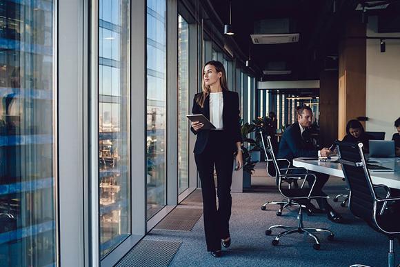 lady walking along glass wall window of office and people working on desks