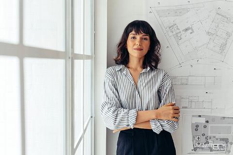 female architect standing next to window with building plans on the wall